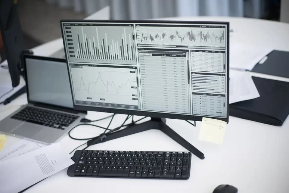 A desk with a monitor and laptop showing charts side by side