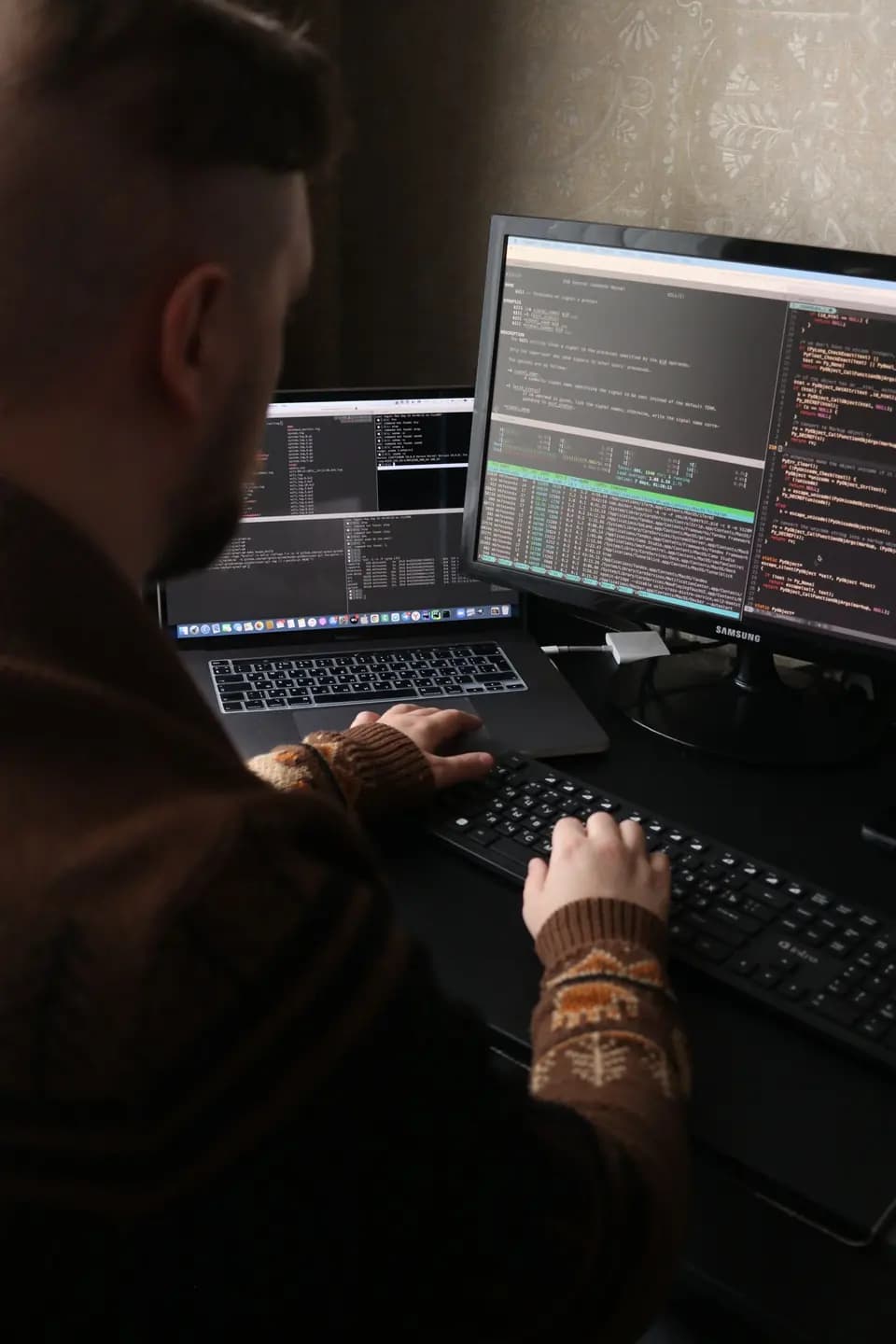 A developer typing at a desk with two monitors and a laptop