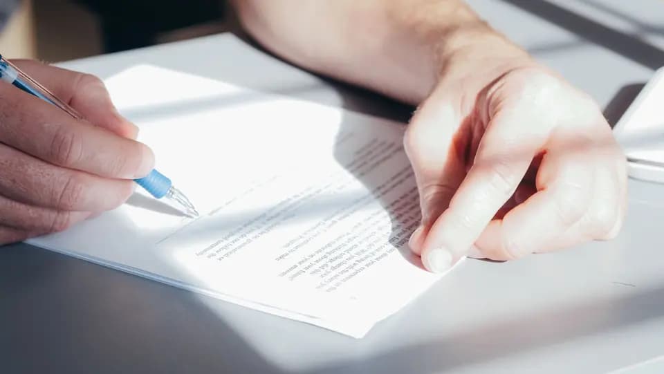 Two hands completing an agreement with a blue pen
